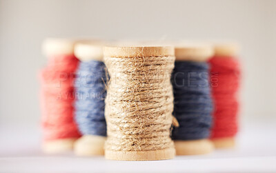 Many rolls of coloured yarn or string lined up in a row in studio isolated against a grey background. For the production of textiles, sewing, crocheting, knitting, weaving, embroidery or rope making