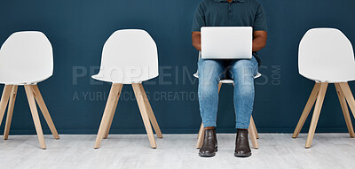 African american businessman typing on a laptop while sitting on a chair in a waiting room. African american businessperson using a laptop in a modern office while waiting in a line alone