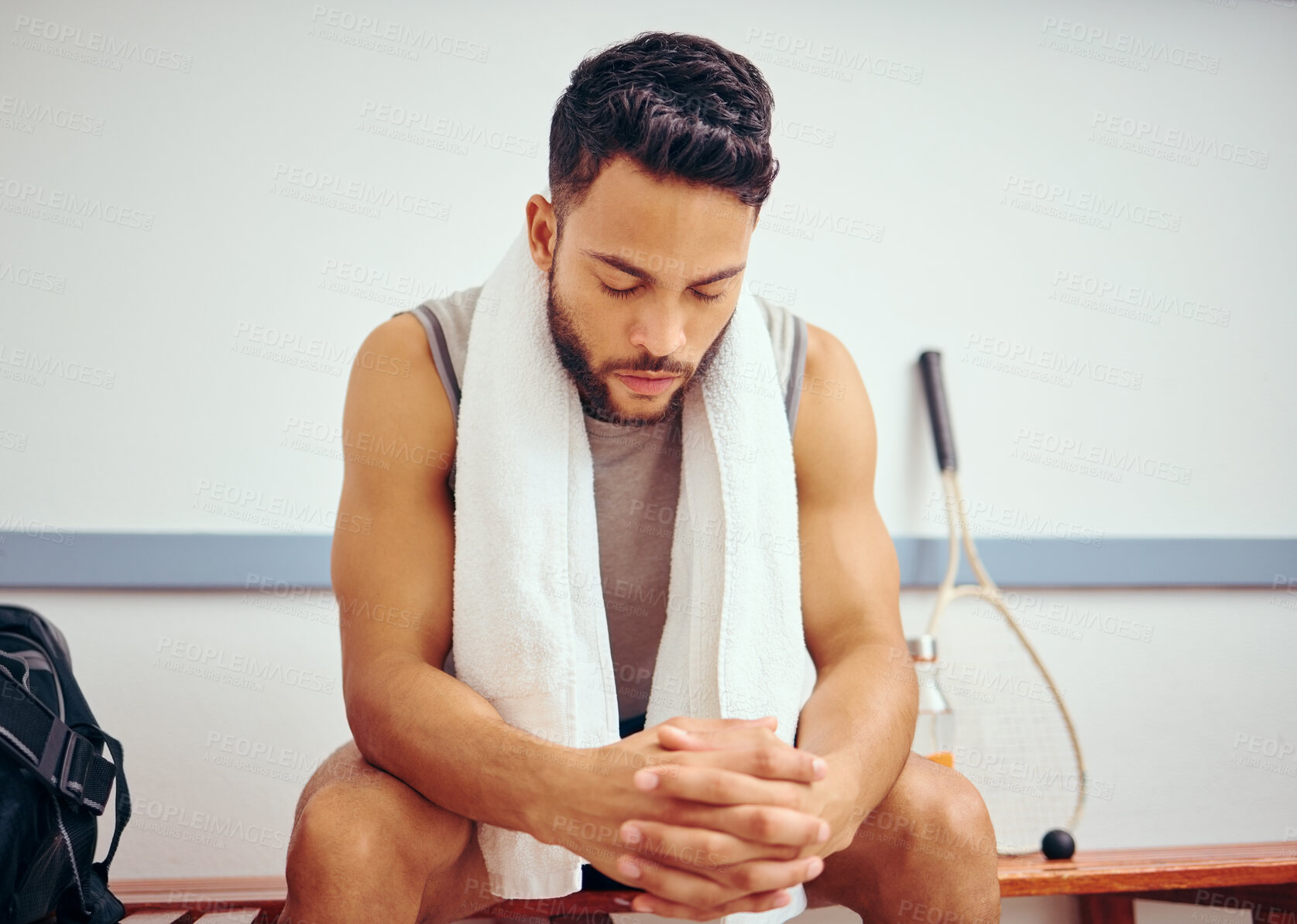 Buy stock photo Hispanic player with his eyes closed in a locker room. Young man sitting and thinking in a gym. Athlete getting ready before a match. Fit man preparing for a match at the gym