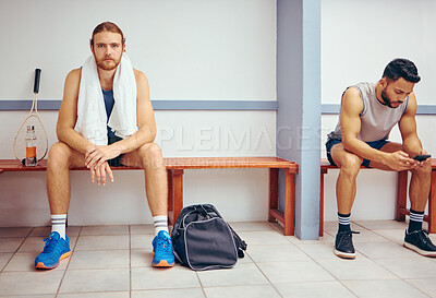 Portrait of a caucasian athlete sitting in a locker room. Two men sitting in a gym locker room together. Serious player relaxing in a gym together. Professional players resting together
