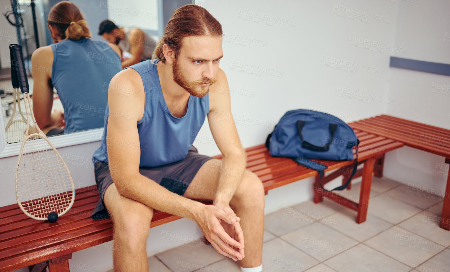 Buy stock photo Caucasian player sitting in a locker room with his squash racket. Two players resting together in a gym locker room. Fit young athlete sitting in a locker room thinking about his match