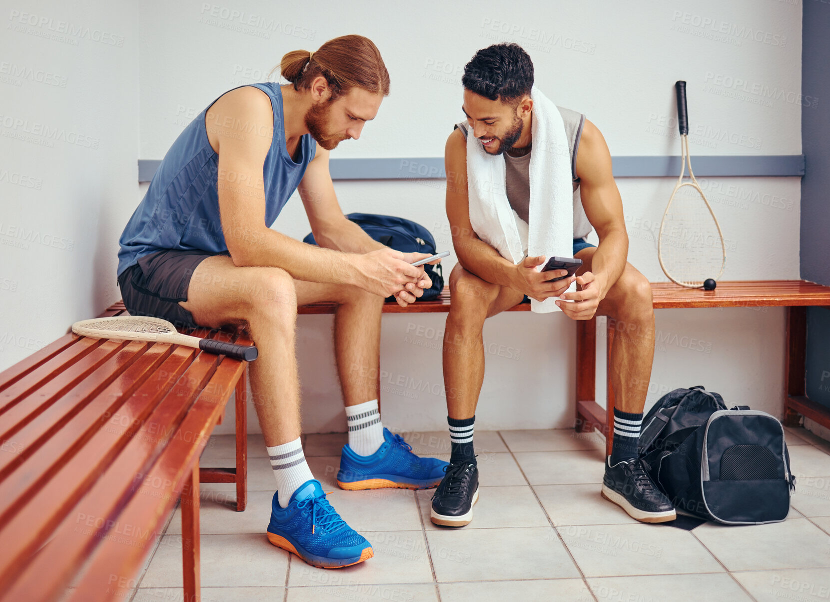 Buy stock photo Two players bonding in their gym locker room. Two professional athletes using their cellphones together. Professional squash players talking and using their smartphones to text in the locker room