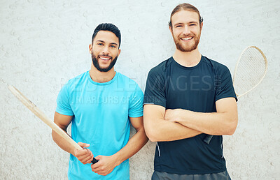 Portrait of two squash players smiling and holding rackets before playing court game with copyspace. Fit active mixed race and caucasian athletes together before training practice in sports centre
