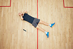 Above view of one unknown athletic squash player lying and covering face with hands after playing on court. Fit active caucasian athlete feeling sad after mistake in training practice in sports centre