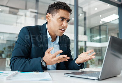 Buy stock photo Young confused mixed race businessman making a hand gesture while upset and working on a laptop at work. One hispanic businessperson looking stressed looking at a laptop in an office