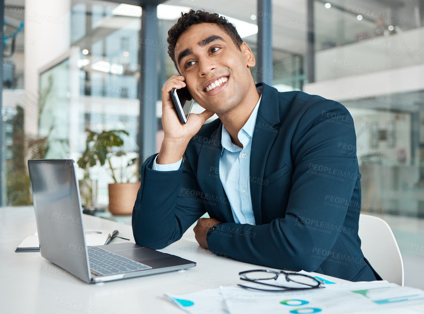 Buy stock photo Young happy mixed race businessman talking and thinking on a call using a phone and working on a laptop alone at work. One cheerful hispanic male businessperson smiling while talking on a cellphone and using a laptop in an office