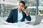 Young serious mixed race businessman talking on a call using a phone and reading a report alone at work. One hispanic male businessperson talking on a cellphone and looking at a document in an office