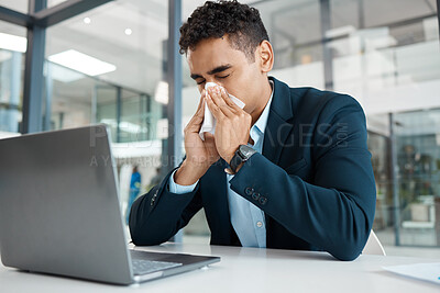 Buy stock photo Sick mixed race businessman blowing his nose with a tissue while working on a laptop alone at work. One hispanic male businessperson suffering from allergies blowing his nose in an office