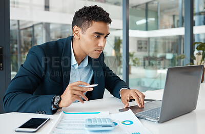 Buy stock photo Young serious mixed race businessman working on a laptop alone at work. Hispanic male businessperson using a laptop and going through a document while working in an office