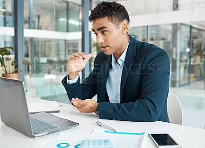 Young serious mixed race businessman talking on a video call using a laptop alone at work. One focused hispanic businessperson talking on a virtual call in an office