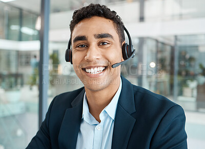 Portrait of a young happy mixed race male call center agent answering calls while wearing a headset alone at work. One hispanic male secretary smiling while talking on a call at a desk in an office