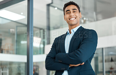 Young happy mixed race businessman standing with his arms crossed alone at work. One confident hispanic male boss smiling and standing in an office
