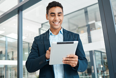 Buy stock photo Young cheerful mixed race businessman holding and working on a digital tablet alone at work. One happy hispanic male businessperson smiling and using social media on a digital tablet in an office