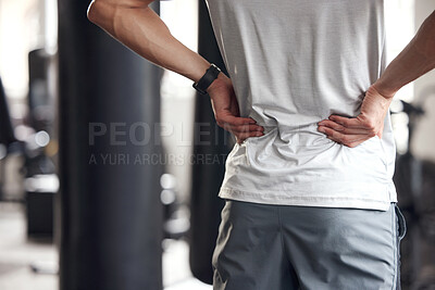 Closeup of one mixed race man holding his sore lower back while exercising in a gym. Guy suffering with painful spine injury from fractured joint and inflamed muscles during workout. Struggling with stiff body cramps causing discomfort and strain