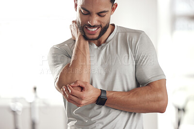 One young hispanic man holding his sore elbow while exercising in a gym. Guy suffering with painful arm injury from fractured joint and inflamed muscles during workout. Struggling with stiff body cramps causing discomfort and strain