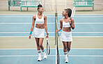 Happy young players walking by the net on the tennis court. African american girls talking after a tennis match. Fit athletes talking, carrying their rackets after a match at the club