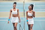 carefree young girls talking after a tennis match. Two professional athletes holding their tennis rackets on the court. Young women walking by the net on the tennis court after practice