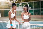 Two friends talking and laughing after a tennis match. Young women bonding after a game of tennis. Professional tennis players walking next to the net on the court. Girls bonding after a game
