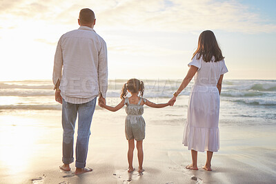 Buy stock photo Rearview cute mixed race girl standing hand in hand with her mom and dad in the sea at the beach. A young couple and their daughter holding hands while standing in the water and looking at a sunset