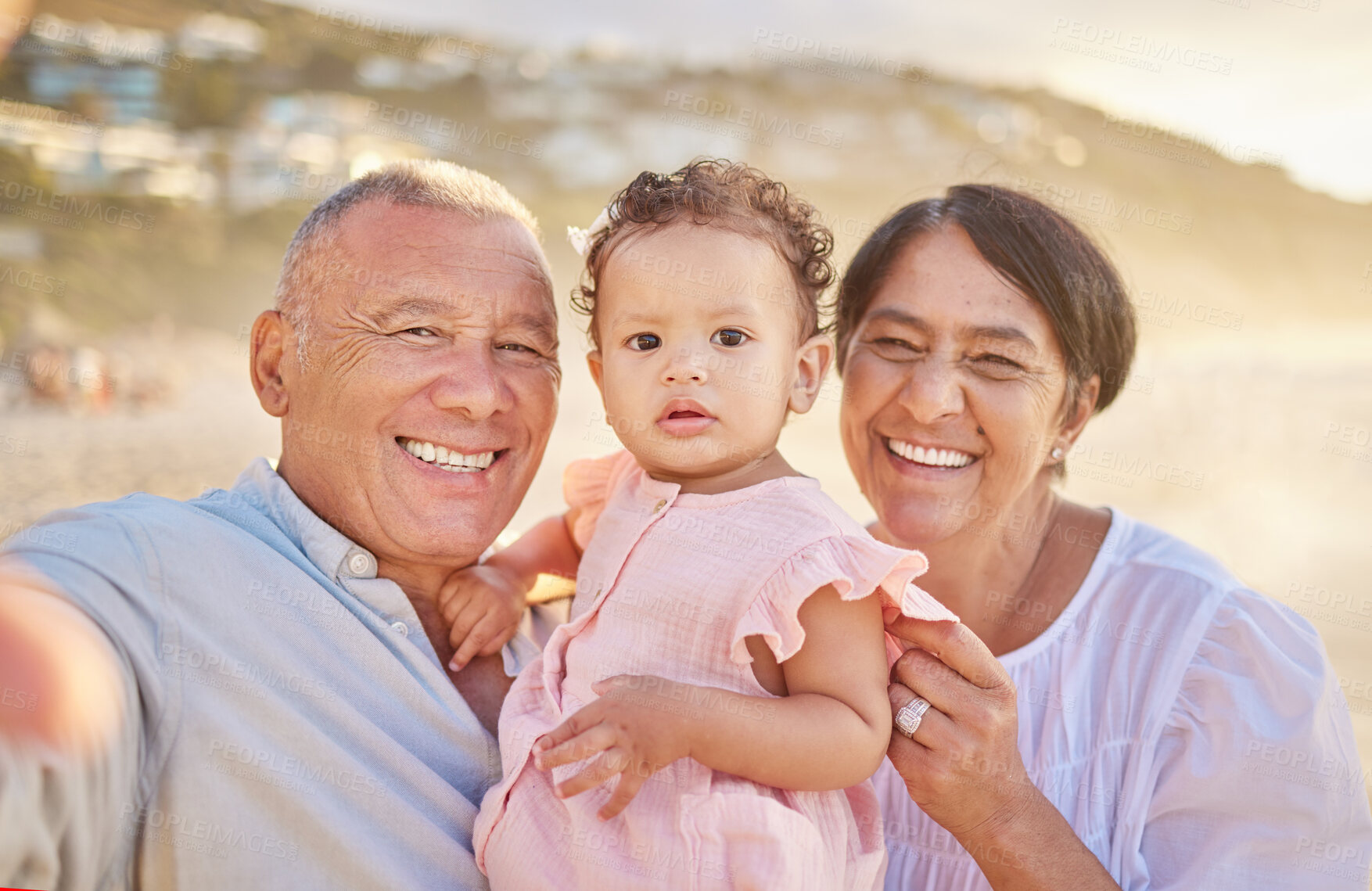 Buy stock photo Mature mixed race couple and their granddaughter taking a selfie photograph at the beach. Cute little girl spending time with her grandfather and grandmother. Happy grandparents with their grandchild