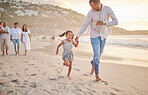 Cute little girl running hand in hand with her mixed race dad on the beach. A daughter and her father holding hands while playing in the sand next to the sea at sunset. Family bonding at the coast
