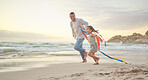 Cute little girl and her mixed race dad flying a kite on the beach. Adorable daughter and her handsome father running and playing in the sand next to the sea at sunset. Family bonding and happiness