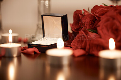 Closeup of romantic engagement ring box, fresh red roses and candles in an empty room at night. Getting ready and prepared for surprise proposal. Loving couple popping the question with sweet gesture