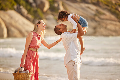 Buy stock photo Full length of a happy mixed race family enjoying family time together at the beach. Loving father lifting his daughter in the air and having fun by the sea while her mother watch. Young couple enjoying vacation by the beach with their little girl