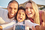Portrait of a mixed race family taking a selfie and smiling outside on a sunny day. Mother and father having fun with their cute daughter at the beach