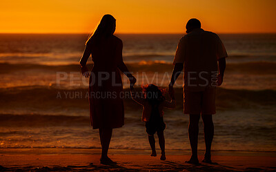 Rearview cute mixed race girl standing hand in hand with her mom and dad in the sea at the beach. A young couple and their daughter holding hands while standing in the water and looking at a sunset