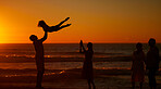 A young family silhouetted on the beach while playing together. Cheerful family with one child, two parents and daughter having fun during sunset at the beach