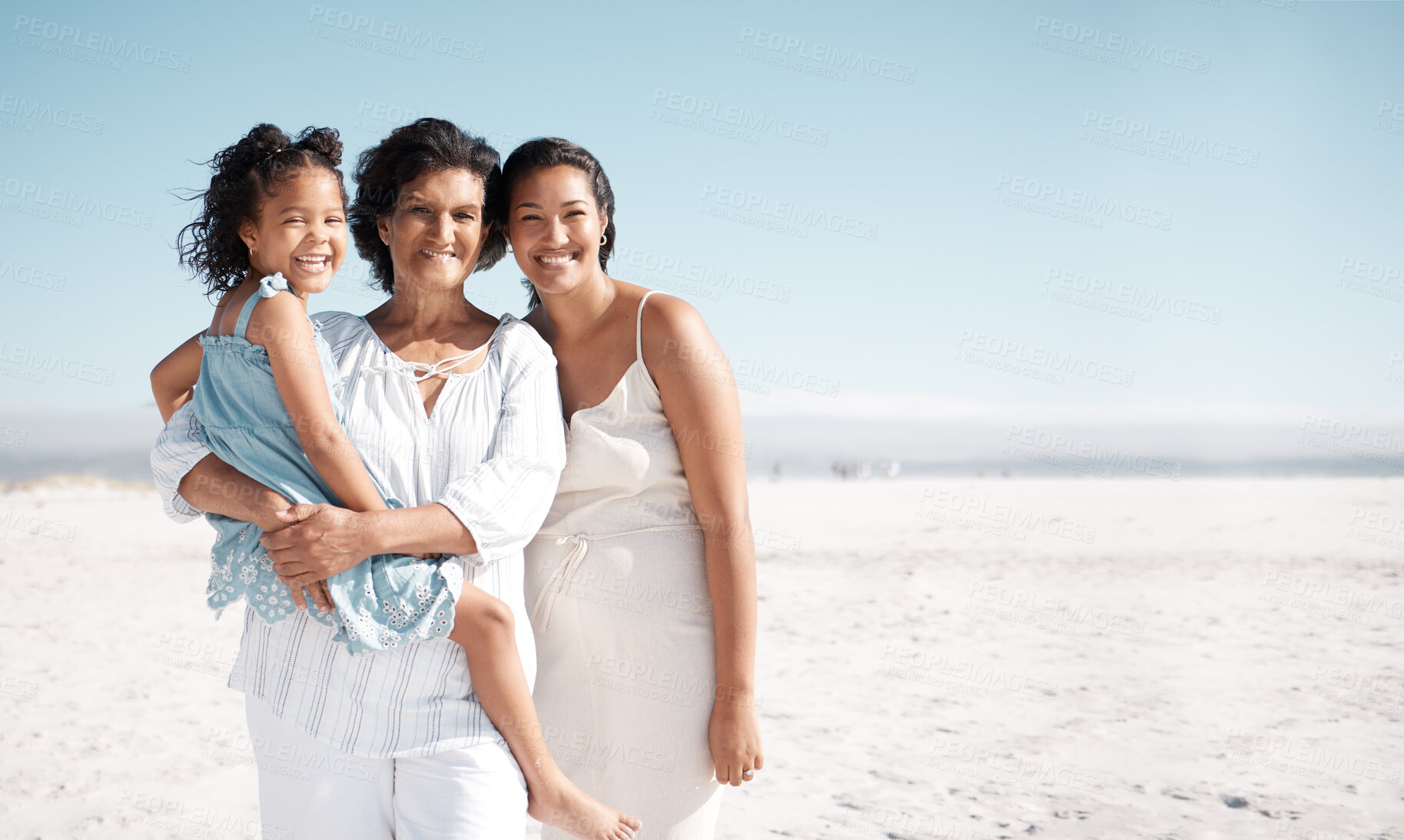 Buy stock photo Smiling mixed race family standing together on a beach with copyspace. Happy hispanic grandmother bonding with granddaughter over weekend. Adorable little girl enjoying free time with single mother