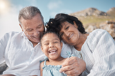 Buy stock photo Smiling mixed race grandparents sitting with granddaughter on a beach. Adorable, happy, hispanic girl bonding with grandmother and grandfather outside on weekend. Seniors and child enjoying free time
