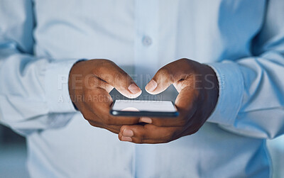 Buy stock photo Closeup hands of african man using a phone while standing in his office. African american business man sending a text message while working late at night at his work. Putting in overtime after hours