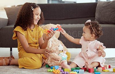 Adorable little mixed race child playing with baby sister in home living room. Two small cute hispanic girls sitting together and bonding while playing with toys and stuffed animals. Smiling siblings