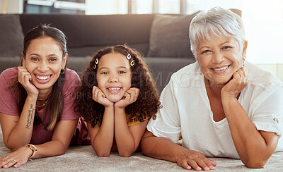 Portrait of mixed race child with single mother and grandmother in home living room. Smiling hispanic girl bonding with parent and senior in lounge. Happy three generations lying together on floor