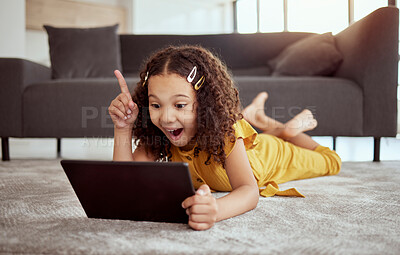Full length adorable little mixed race child using digital tablet and thinking at home. One small cute hispanic girl lying alone on living room floor. Idea and solution while playing technology game