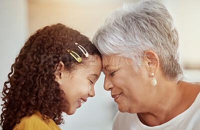 Closeup of mixed race grandmother and granddaughter with foreheads touching at home. Adorable affectionate little girl feeing safe, secure with senior woman in living room. Hispanic child and elderly
