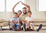 Portrait of a young couple ensuring that their family's home is covered. Hispanic parents smiling and making a roof gesture with their hands over their two sons in the lounge at home