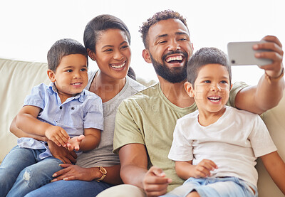 Buy stock photo A mixed race family sitting on a sofa using a smartphone to take a selfie and smiling at home. Young hispanic father taking a photo of his wife and sons on the couch in the living room