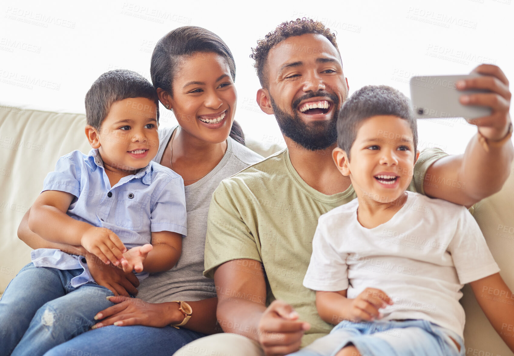 Buy stock photo A mixed race family sitting on a sofa using a smartphone to take a selfie and smiling at home. Young hispanic father taking a photo of his wife and sons on the couch in the living room