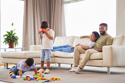 Buy stock photo Young mixed race family bonding in the lounge while the parents relax on the couch while their two little sons play. Hispanic couple smiling while watching their boys playing in the living room