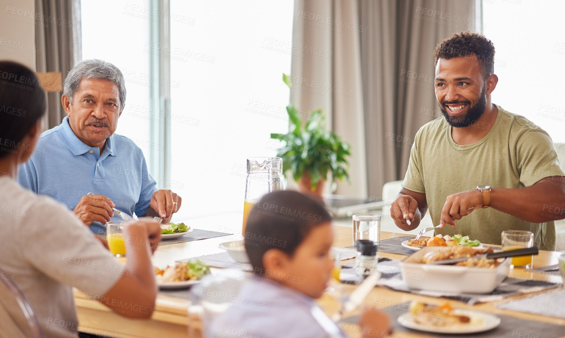 Buy stock photo Closeup of a mixed race family having lunch at a table in the lounge at home and smiling while having a meal together