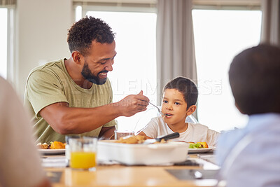 Closeup of a mixed race male and his son enjoying some food at the a table during lunch at home in the lounge. Hispanic father smiling and eating alongside his son at home