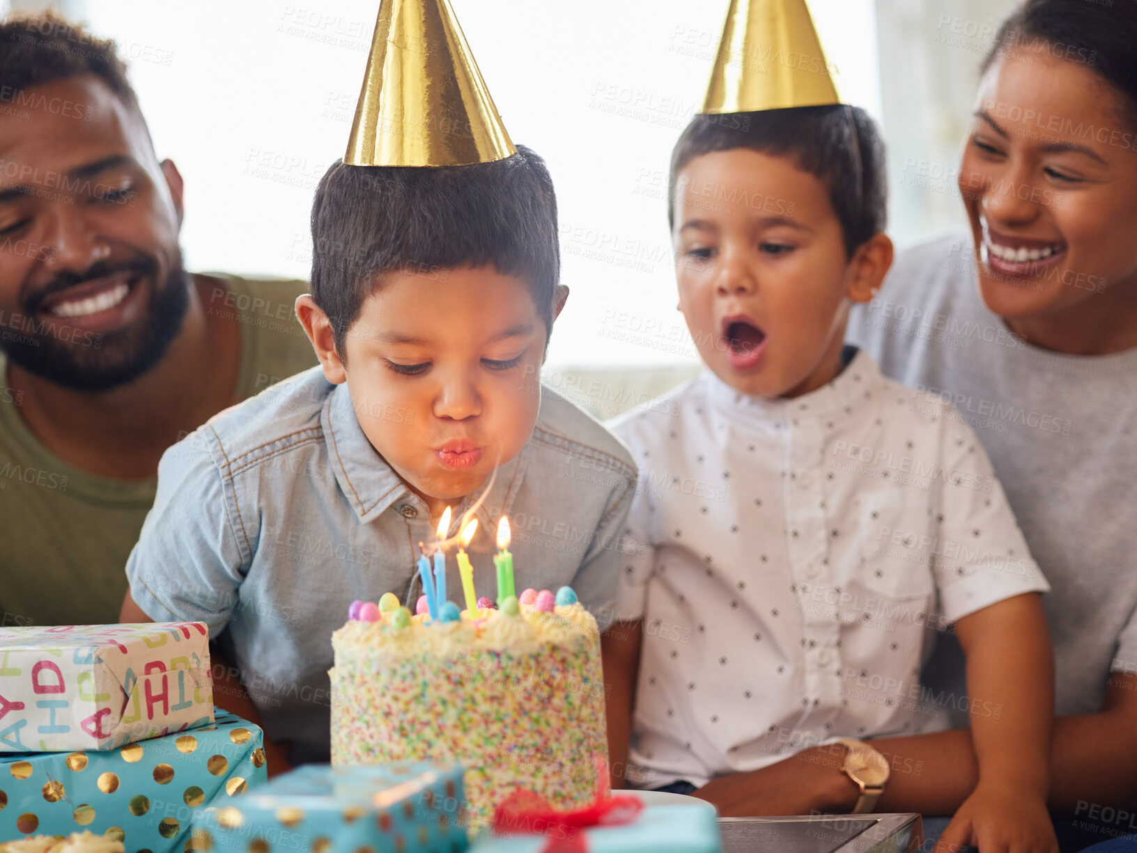 Buy stock photo Closeup of a little mixed race boy blowing the candles on a cake at a birthday party with his little brother and parents smiling and watching. Cute hispanic boy celebrating his birthday with his family at home