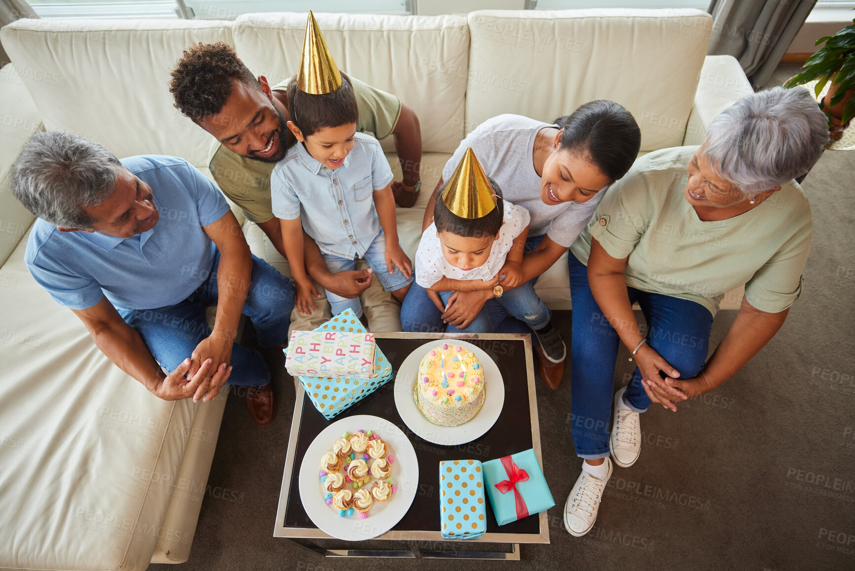Buy stock photo Closeup of a little mixed race boy blowing the candles on a cake at a birthday party with his little brother, parents  and grandparents smiling and watching. Cute hispanic boy celebrating his birthday with his family at home