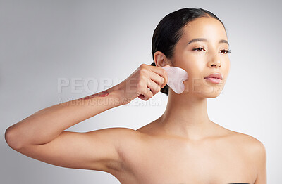 A beautiful mixed race woman using a rose quartz gua sha for deep penetration cell renewal. Young hispanic woman using anti ageing tool against grey copyspace background