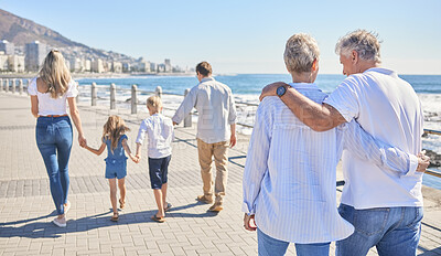 Buy stock photo Rear view of a senior couple strolling on a seaside promenade while their children and grandchildren walks ahead.