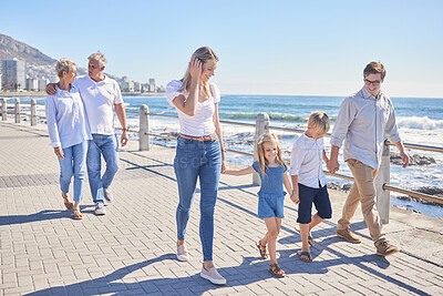 Loving caucasian parents holding hands with their little daughter and son while their grandparents follow in the background. Happy multi-generation family walking along seaside promenade on a sunny day