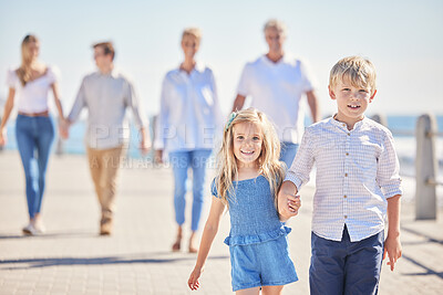 Buy stock photo Adorable little sibling brother and sister holding hands while walking ahead on a seaside promenade while their parents and grandparents follow on a sunny day. Multi-generation family spending time together while on holiday
